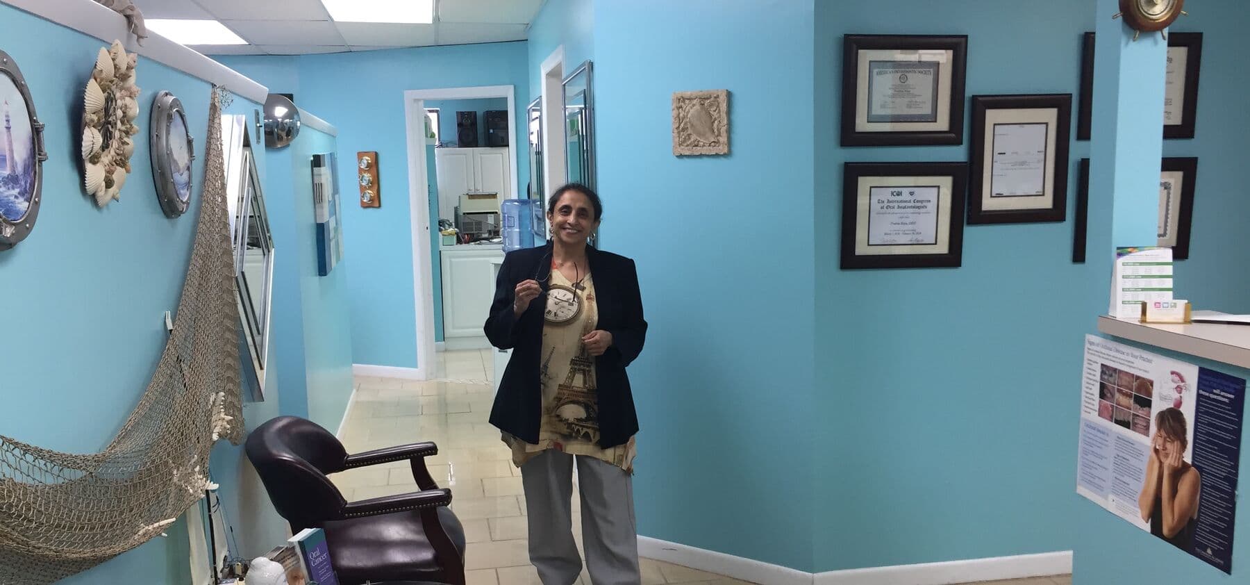 Dr. Prabha Raju in the hallway of Tender Dental Care, with patient certificates on the wall